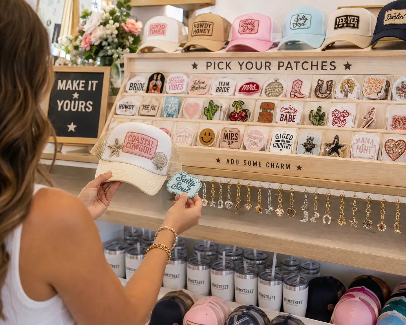 Guest choosing embroidered patches from the Pick Your Patches wall at a Brimstreet hat bar, holding a Coastal Cowgirl trucker hat